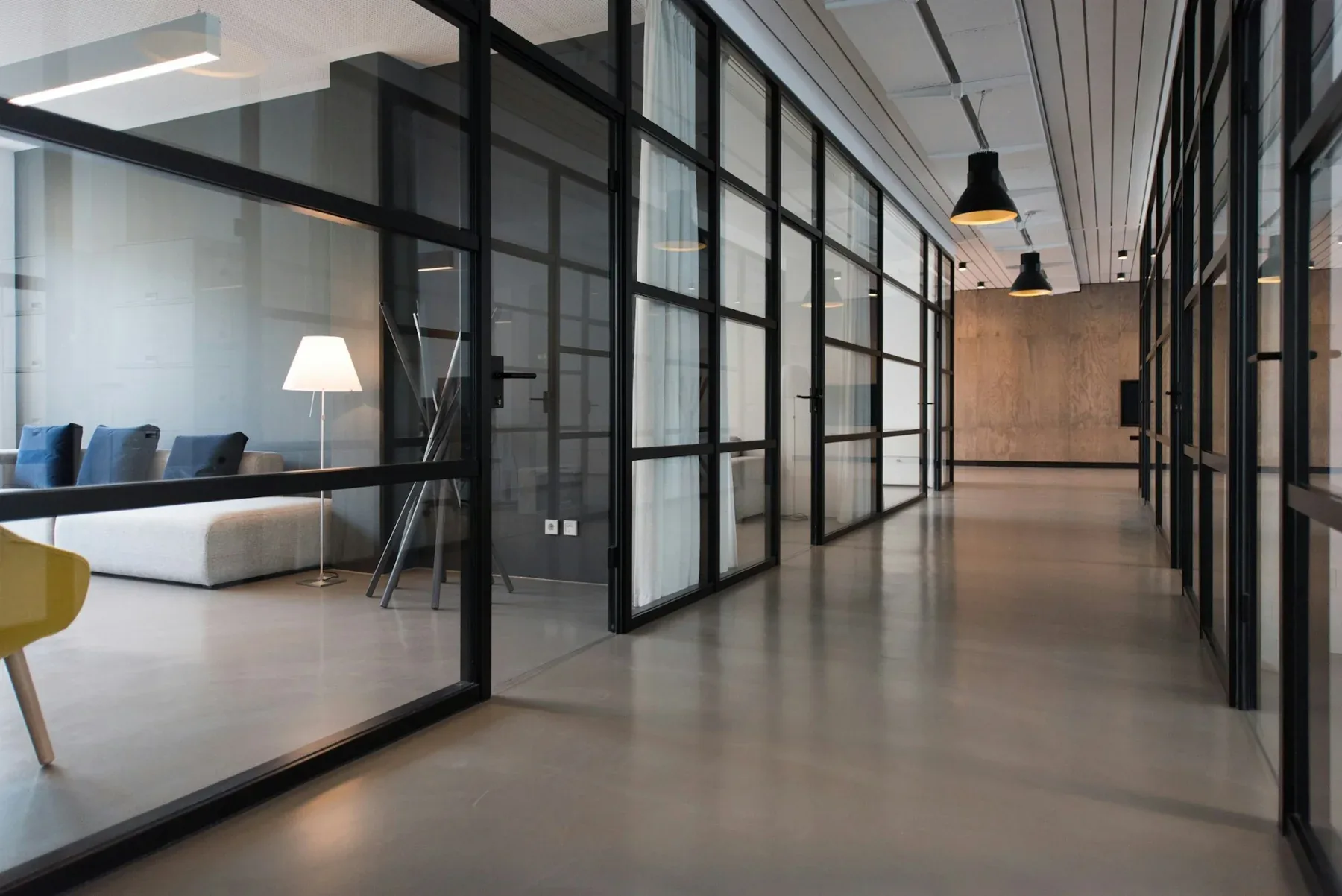 Glass-partitioned office lounge with a gray sofa and tall windows